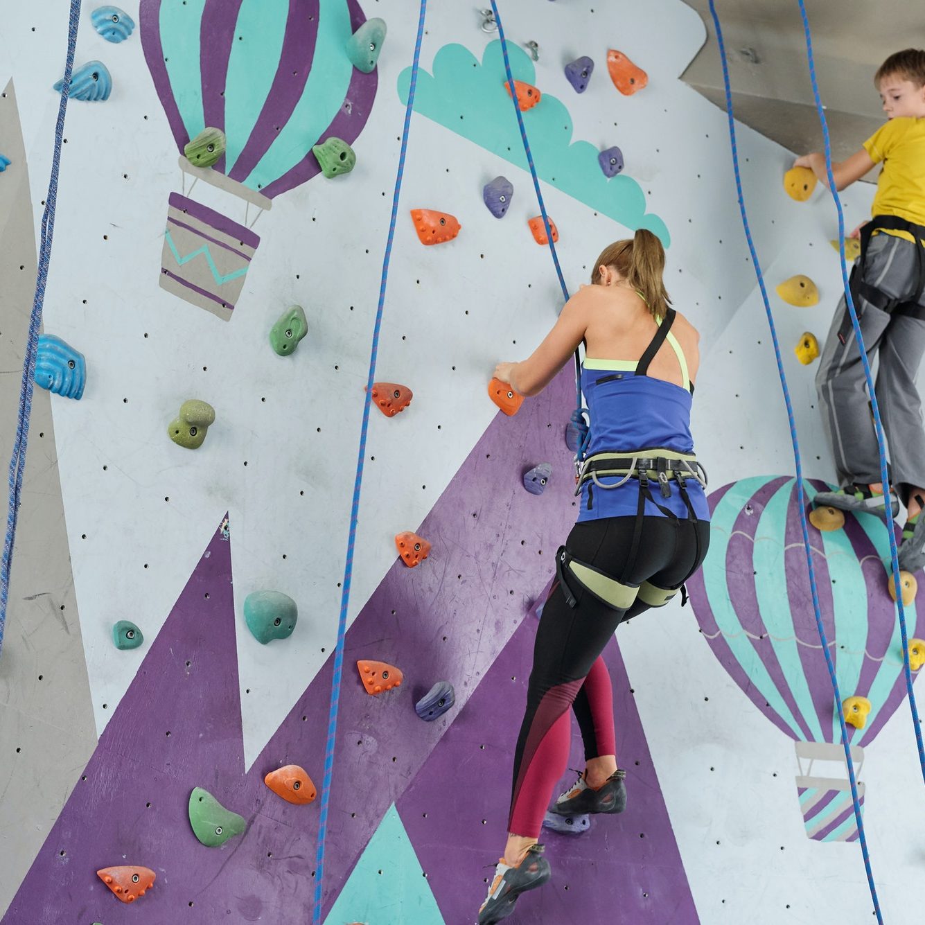 Blonde girl and schoolboy grabbing by small rocks on climbing equipment
