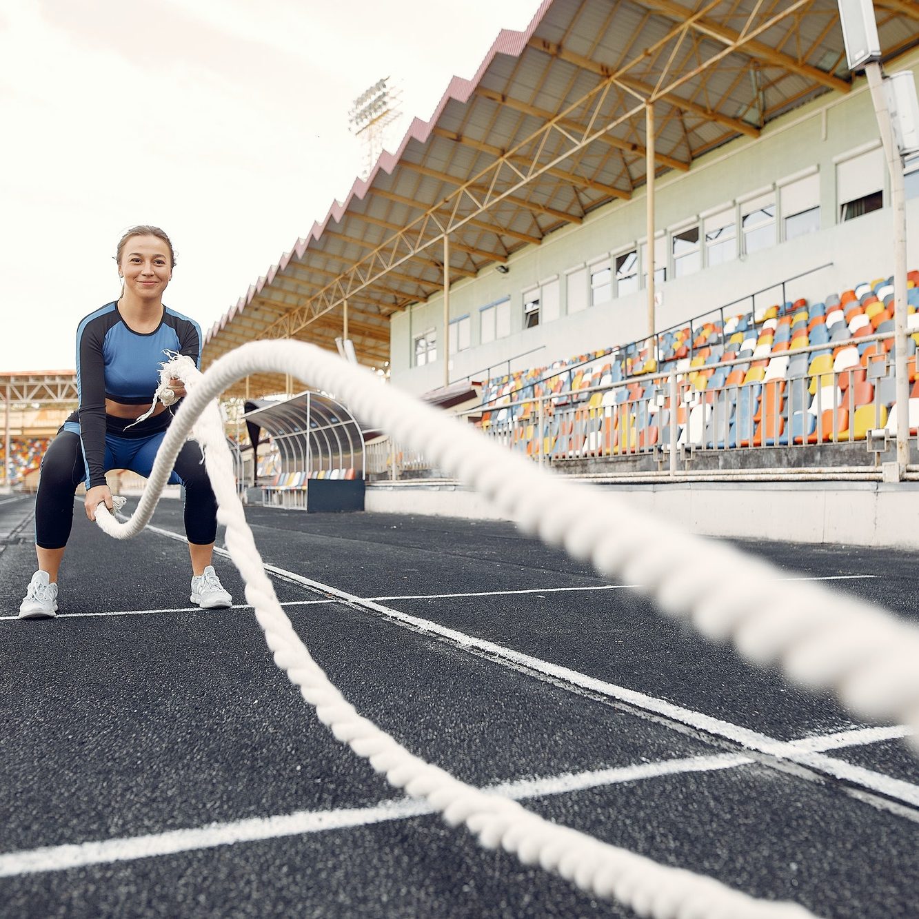 Sports girl in a blue uniform training at the stadium with rope