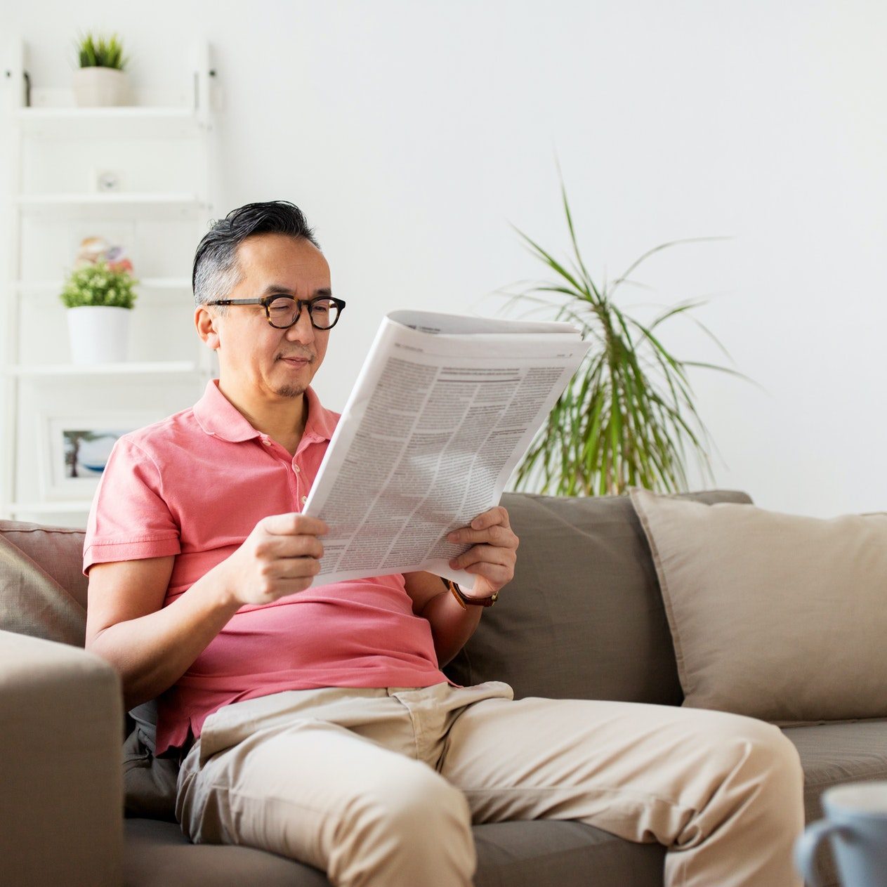 asian man in glasses reading newspaper at home