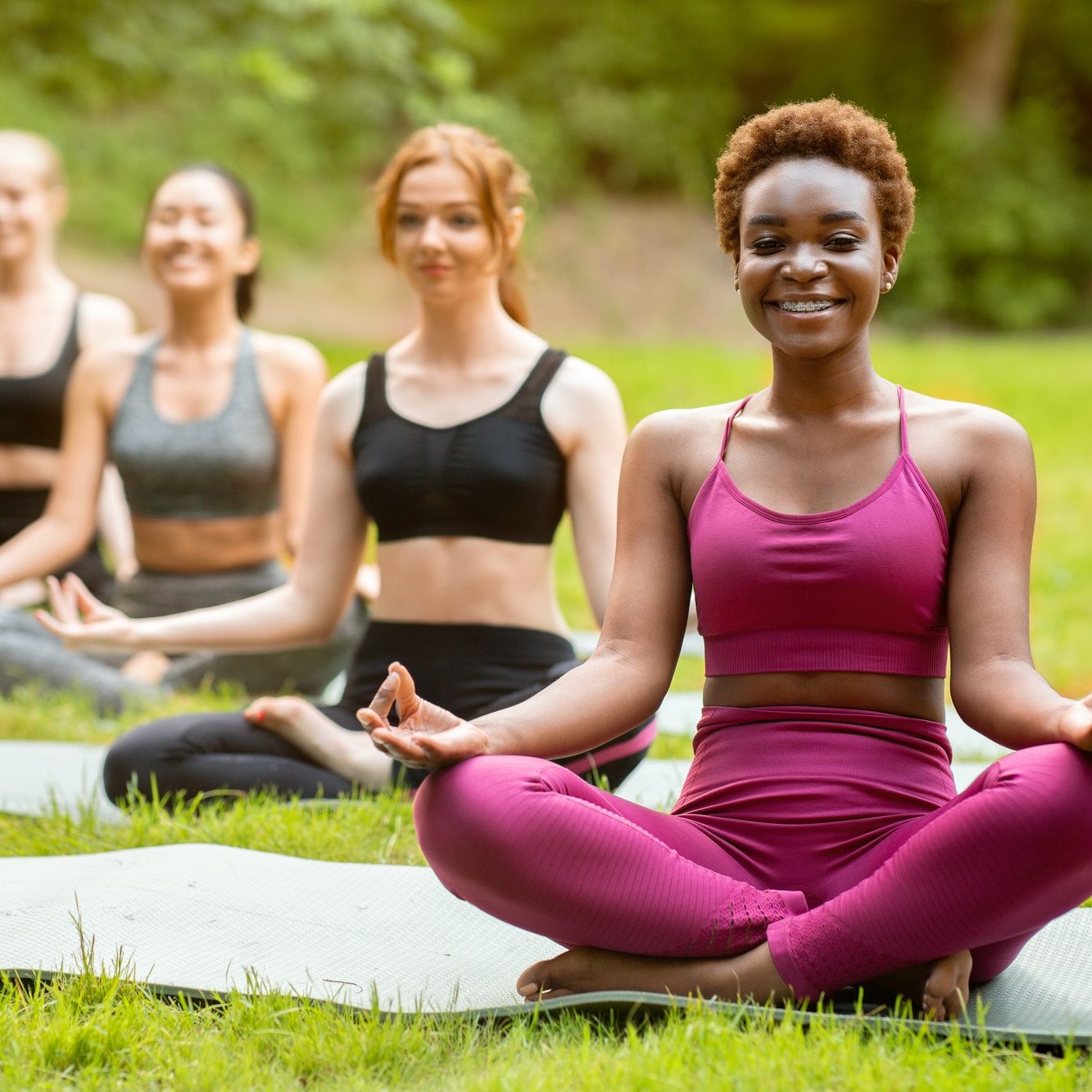 Beautiful black woman with her friends meditating on group yoga class at park, copy space