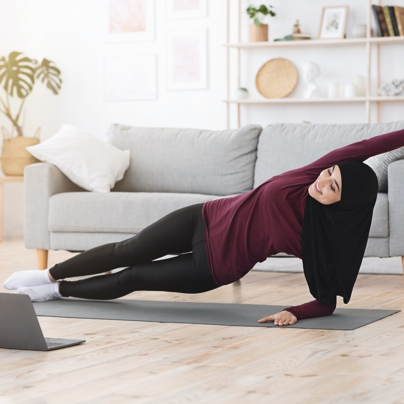 Sporty muslim woman doing side plank exercise in front of laptop at home