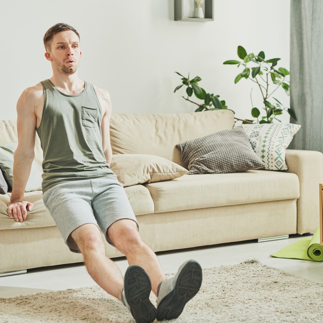 Young active man holding by couch behind his back while doing difficult exercise